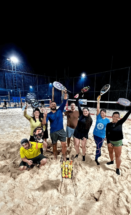 Turma posa com raquetes na quadra de areia da Arena Sul.