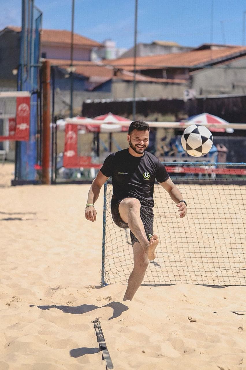 Jogador de futevôlei controla a bola com o pé diante da rede na quadra de areia.